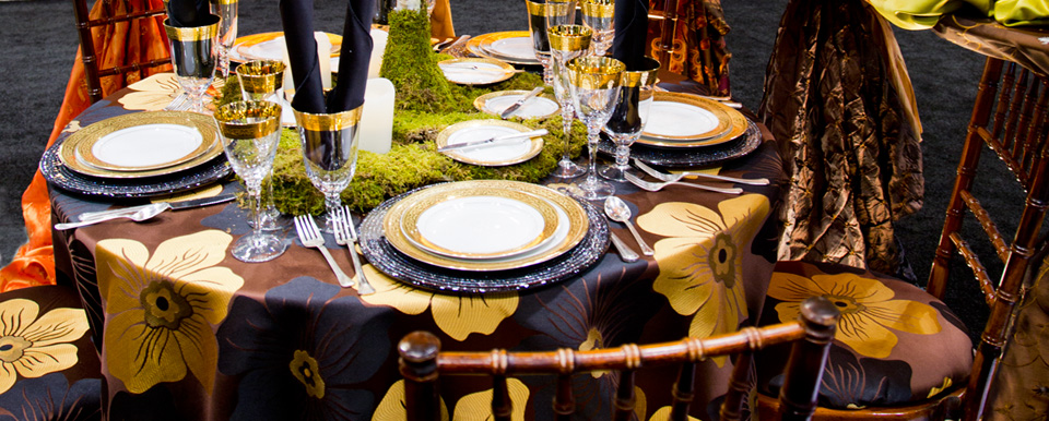 Elegant round table setting with gold-rimmed white plates, crystal glassware, moss centerpiece runner, and floral brown accents